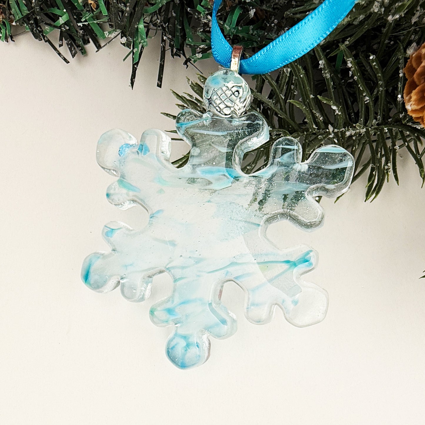 Blue fused glass snowflake ornament with soft blue marbling and a glossy finish, handmade Christmas décor.