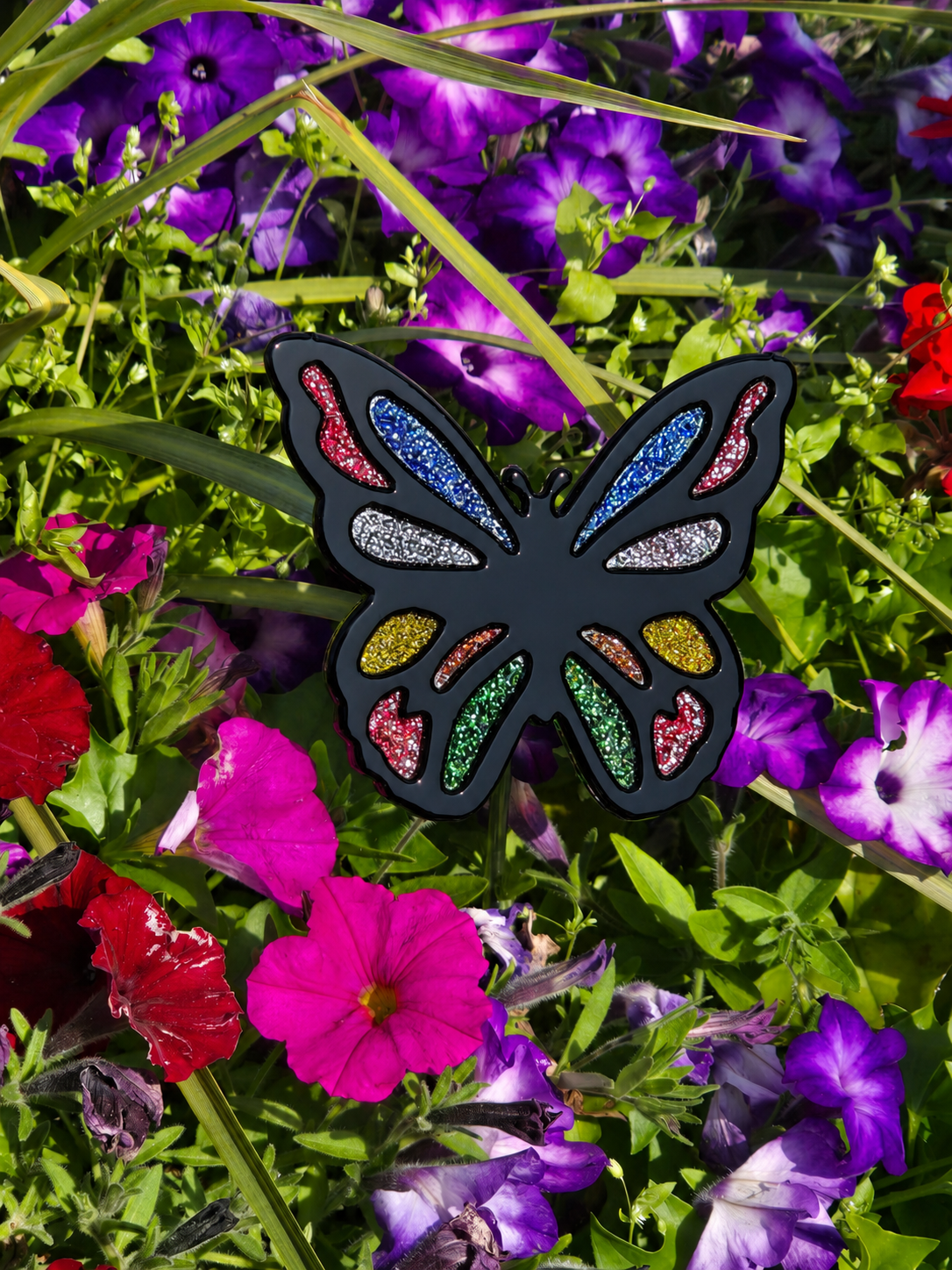 Fused glass butterfly garden stake with black outline and multicolour frit accents displayed among vibrant flowers.