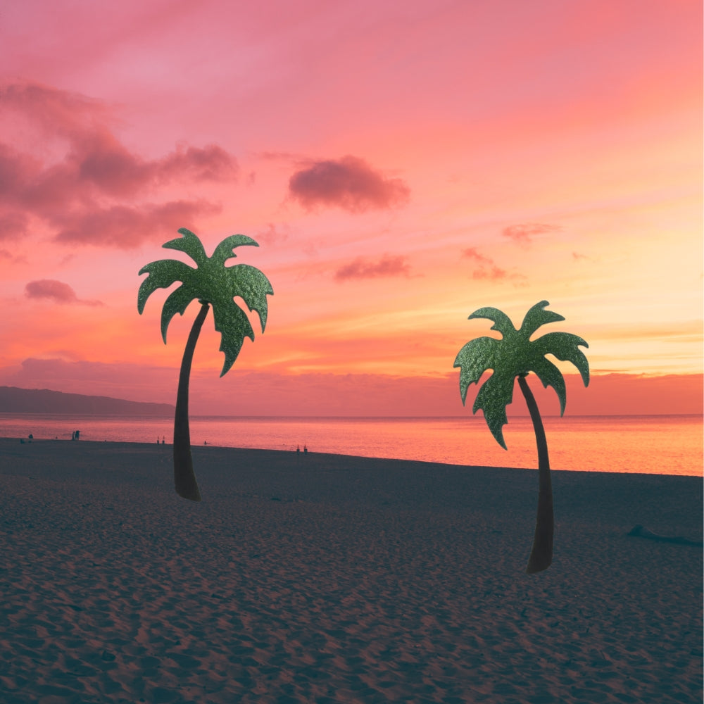Precut glass shape of a palm tree in green and brown glass on a sunset beach.