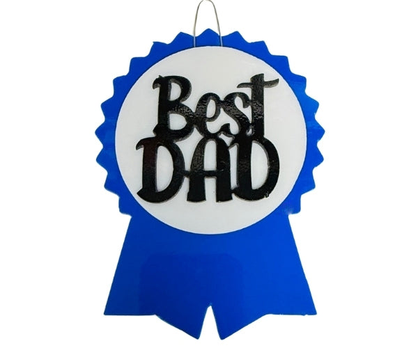 Fused glass Father's Day project featuring a blue ribbon, white circle, and black “Best Dad” cutout, tack fused and ready to hang.