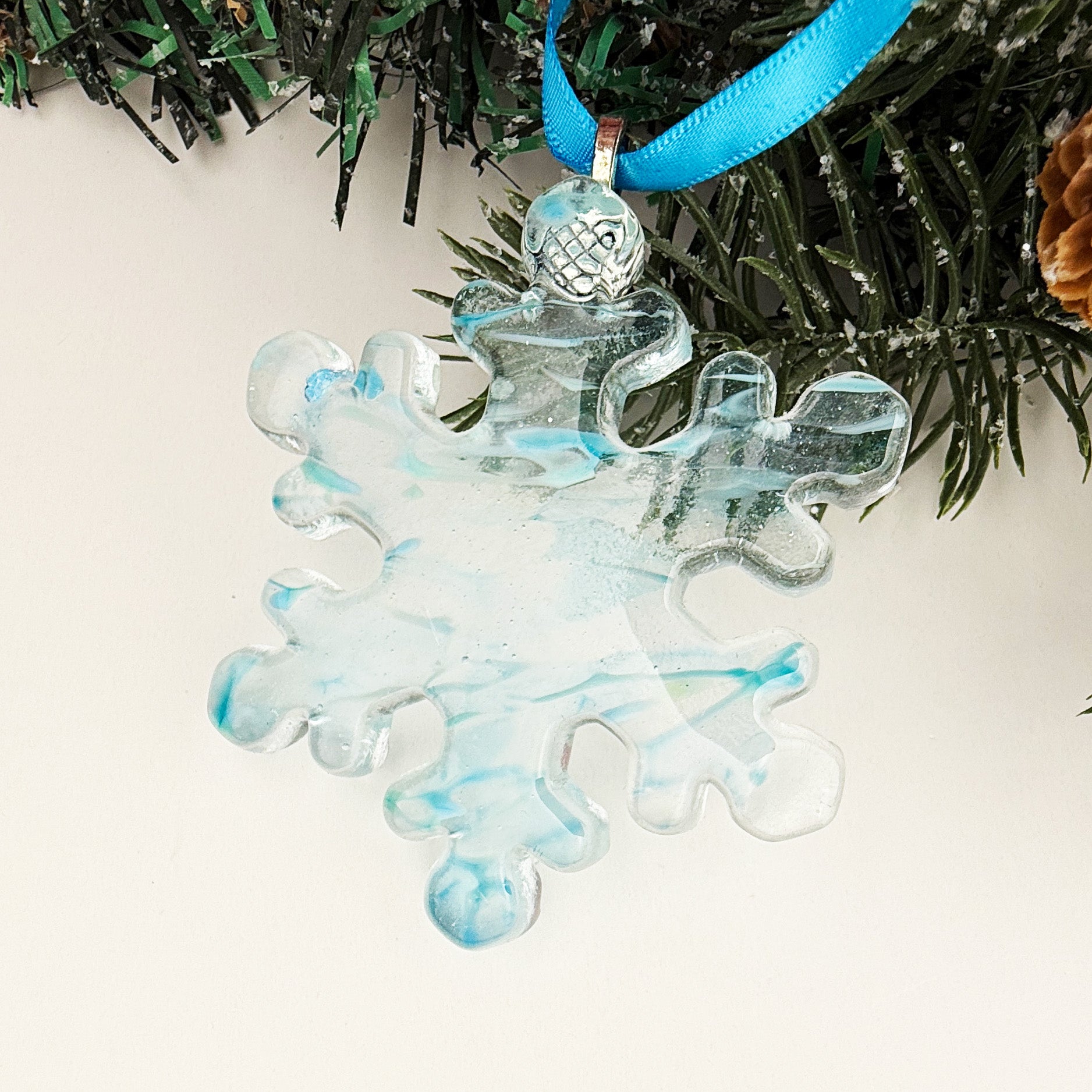 Blue fused glass snowflake ornament with soft blue marbling and a glossy finish, handmade Christmas décor.