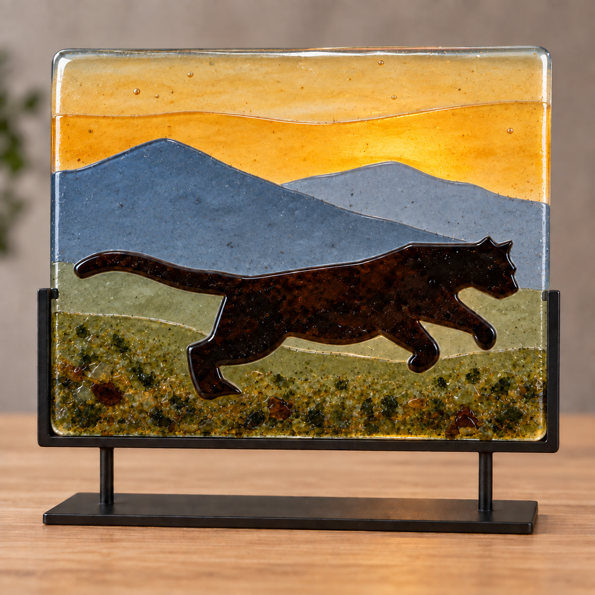 COE 96 fused glass landscape featuring a brown running cougar, layered mountains and frit details displayed in a black metal stand.