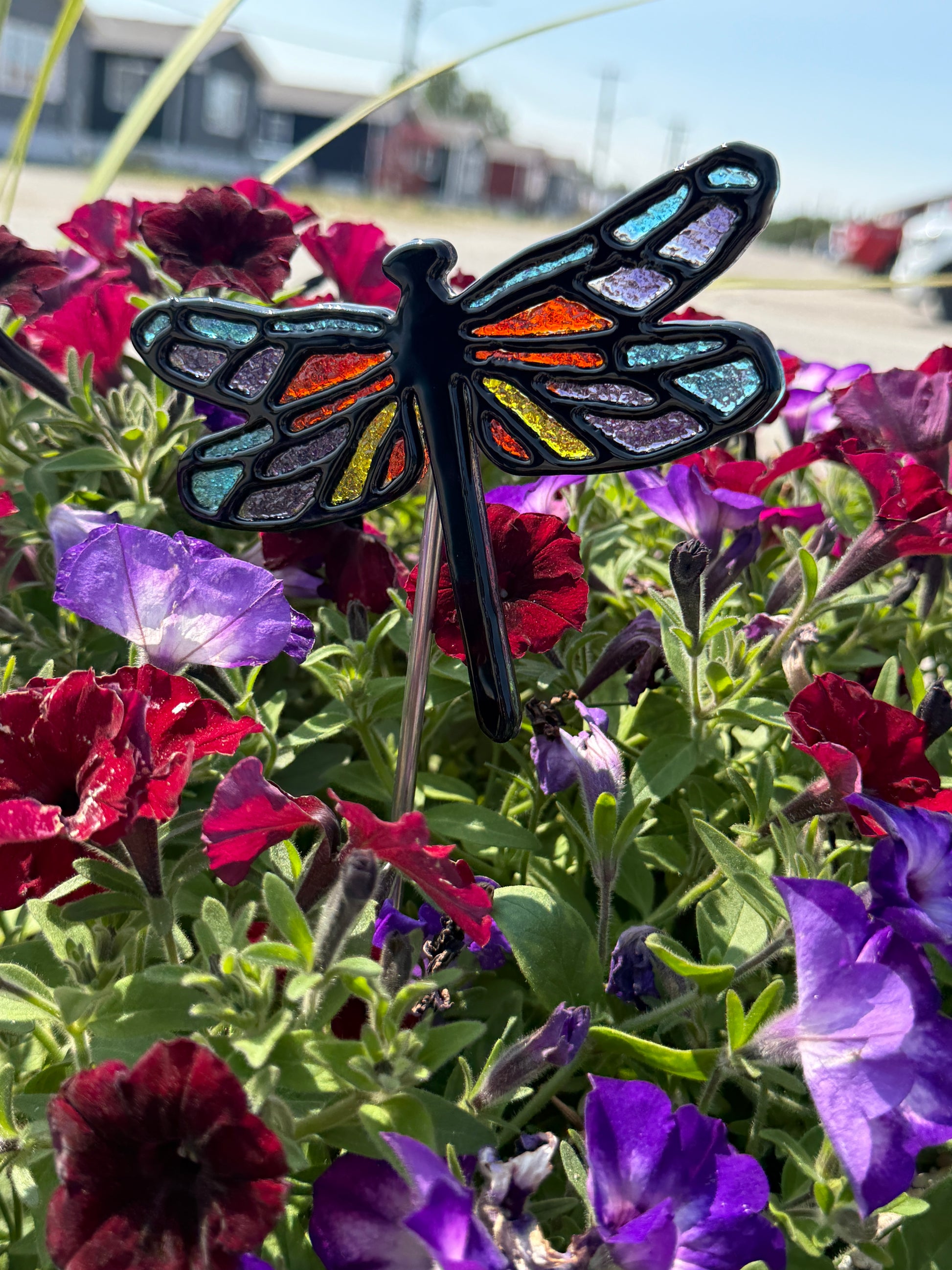 Finished fused glass dragonfly garden stake with blue, orange, yellow and purple frit accents among flowers.