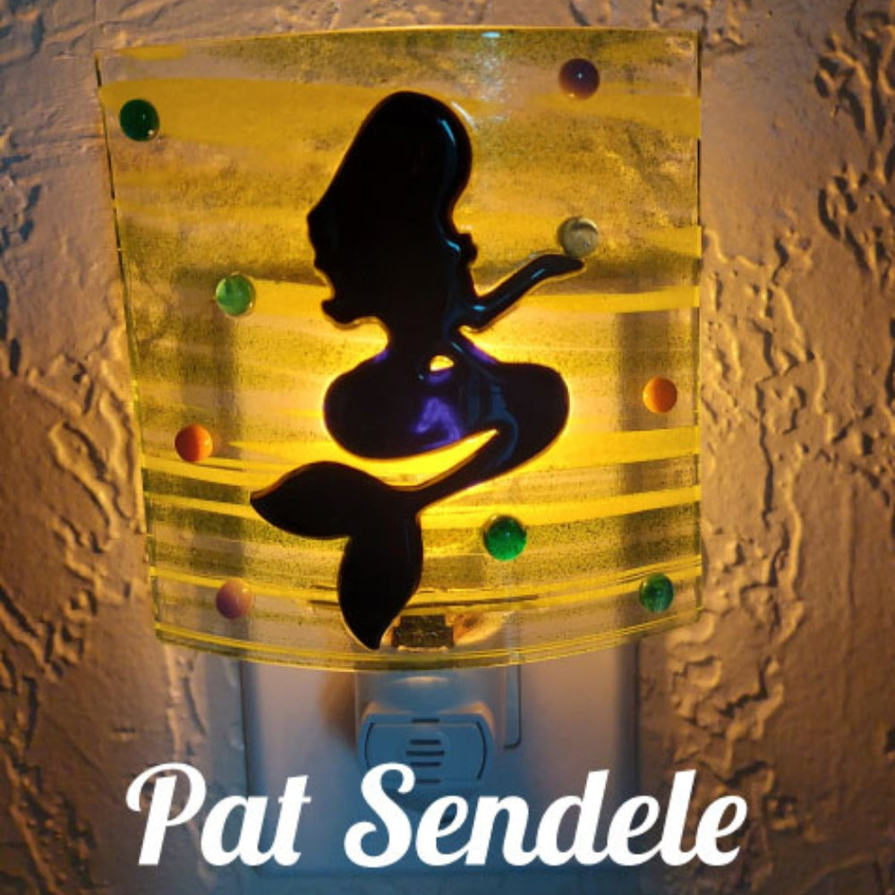 Precut glass shape of a mermaid sitting in an art piece by Pat Sendele.