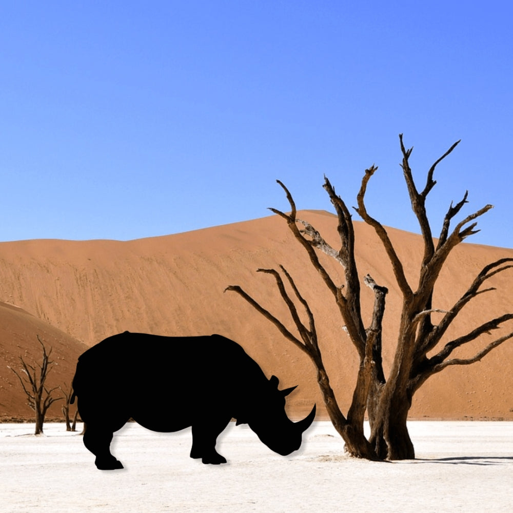 Precut glass shape of a rhino by a desert tree.