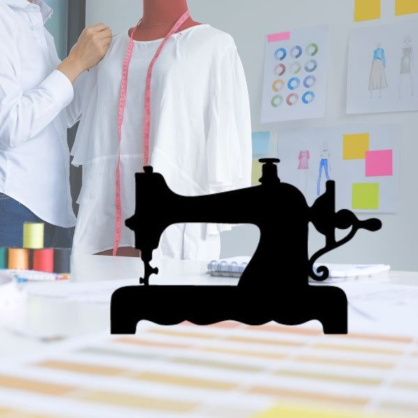 Silhouette of a vintage sewing machine precut in black Bullseye 90 COE glass, overlaid on a background of a modern sewing workspace with wooden spools and white thread.