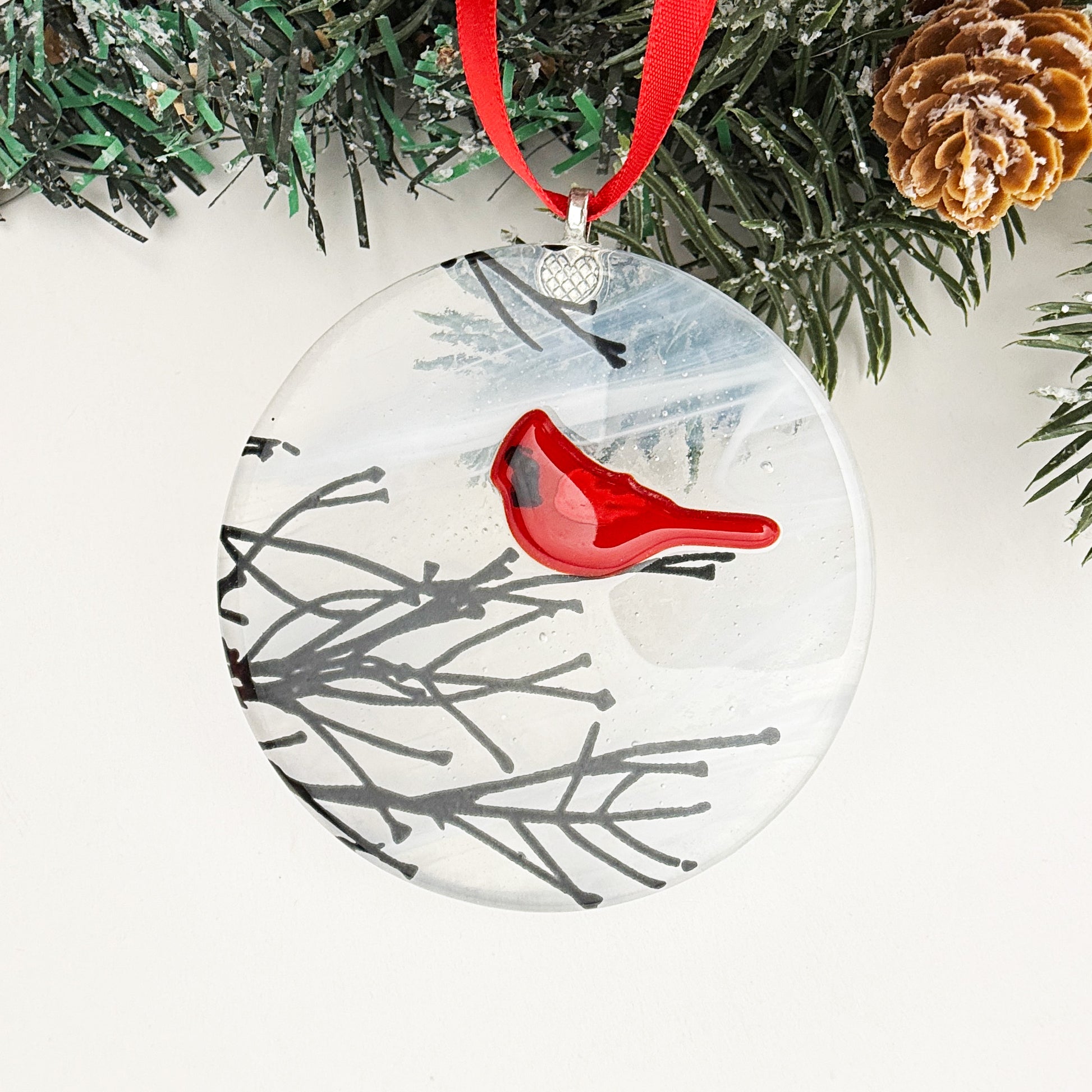 Round Christmas ornament with a red cardinal perched on winter branches, symbolizing love and remembrance.